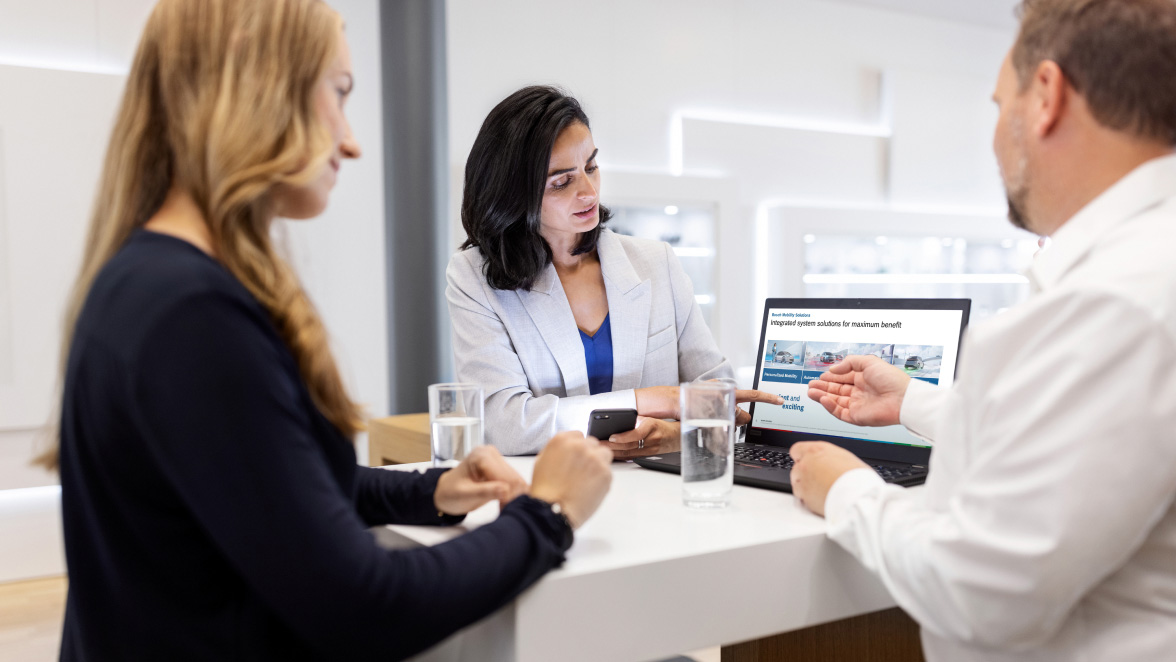 Three people standing around a high table working together on a laptop.